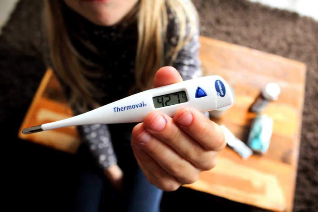 Kind hält Fiebertemometer hoch, das eine hohe Temperatur anzeigt