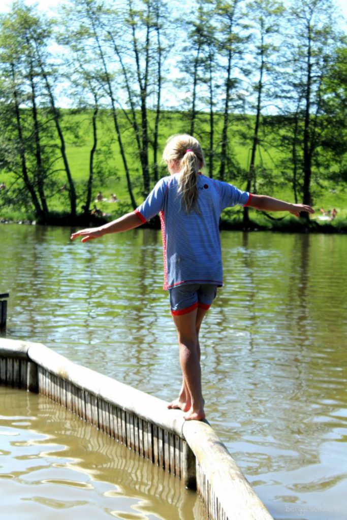 Mädchen balanciert auf einer Planke an einem See