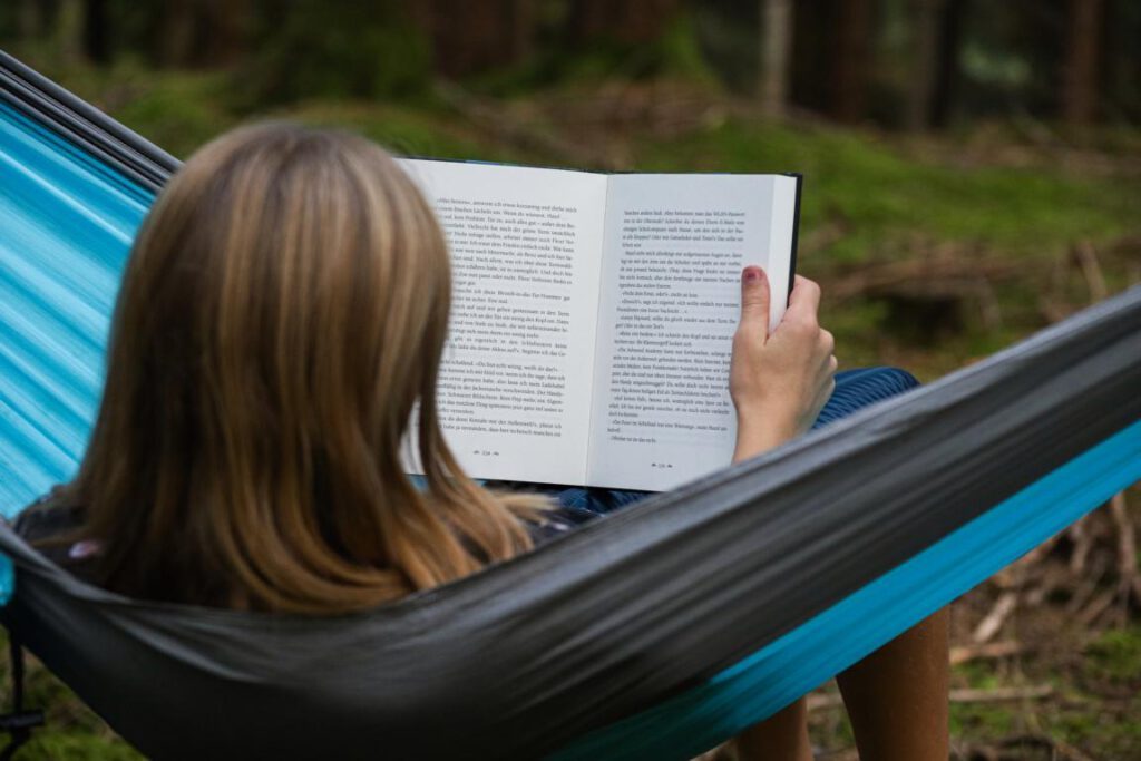 Mädchen im Wald in einer Hängematte und ließt gerade ein Buch