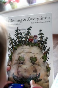 Kind hält das Buch Riesling und Zwerglinde hoch